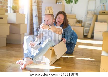 Funny and crazy couple having fun riding a cardboad box as a car, smiling happy and lauging at new home