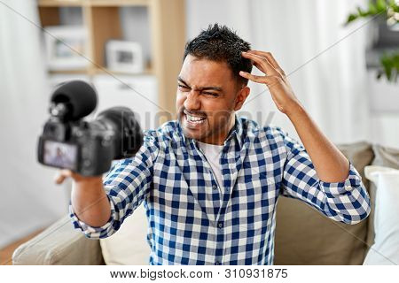 blogging, videoblog and people concept - angry indian male video blogger with camera videoblogging at home