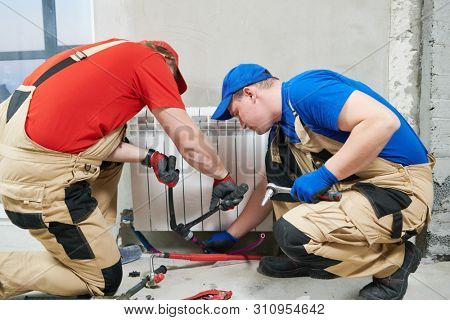 two plumber at work. Installing water heating radiator