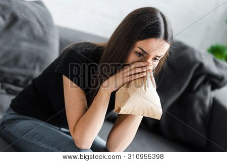 Young Woman Breathing Into Paper Bag While Suffering From Panic Attack At Home