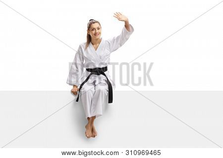 Full length portrait of a young woman in kimono sitting on a panel and waving isolated on white background