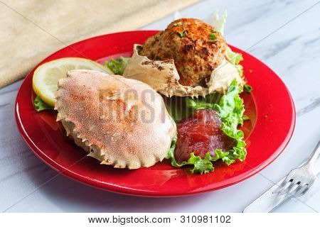 Stuffed Seasoned Crab Shells Garnished With Romaine Lettuce And Sliced Lemon With Cocktail Sauce