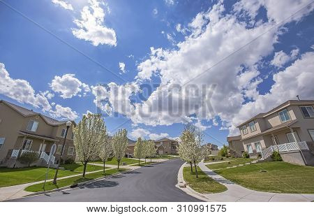 Paved Road And Homes On A Neighborhood Under Cloudy Blue Sky On A Sunny Day
