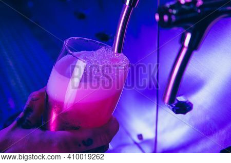 Close-up Beer Glass In Barman Hand In Multicilored Neon Light.