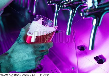 Close-up Beer Glass In Barman Hand In Multicilored Neon Light.