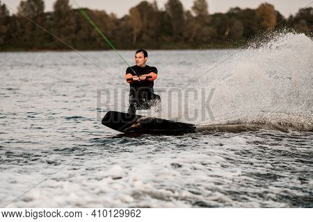 Man Holds Taut Cable In His Hands And Balances On Wave On Wakeboard