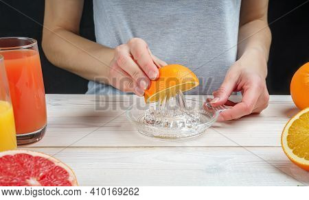 Young Woman Squeezes Orange Juice Using A Manual Glass Juicer