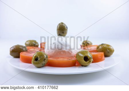 The Meal On A White Plate On A White Background Consists Of Sliced Tomatoes, Pitted Olives And Mozza