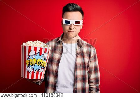 Young handsome caucasian man wearing 3d movie glasses and eating popcorn Relaxed with serious expression on face. Simple and natural looking at the camera.