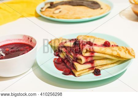 Blini Pancakes With Red Berry Jam Close-up On A Blue Plate On A Light Background . Traditional Russi