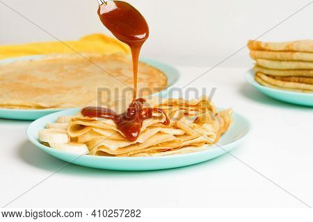 Blini Pancakes With Caramel, Dripping On A Spoon Levitation Close-up On A Blue Plate On A Light Back