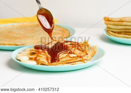 Blini Pancakes With Caramel, Dripping On A Spoon Levitation Close-up On A Blue Plate On A Light Back