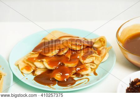 Blini Pancakes With Caramel, Dripping On A Spoon Levitation Close-up On A Blue Plate On A Light Back