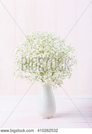 Bouquet of Gypsophila flowers in porcelain white  vase against a light pale  pink wooden background. Selective focus.