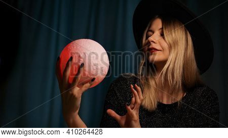 A Young Woman Fortune Teller In A Hat Is Holding A Magic Ball. Beautiful Psychic Woman Is Guessing W