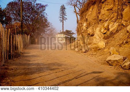 Local Bus Riding Through Dust On Dirt Road Along Mountains With Rockslide During Sunset, San Pedro L
