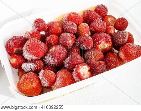 Close Up Of Frozen Strawberries With Frost On Them In A Plastic Container On White Background