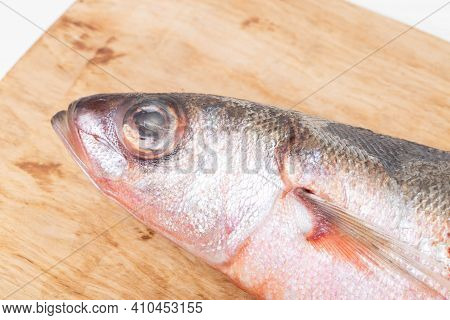 Red-eyed Sea Fish On A Wooden Kitchen Board On A White Background, Isolate. Close-up, Macro, Studio 