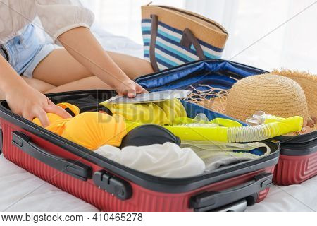 Close-up Female Hands Packing Summer Clothes And Beach Accessories Into Suitcases On Bed. Preparing 