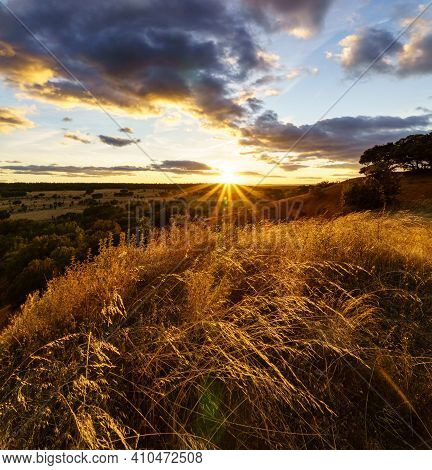 Sunset Landscape In The Field, Trees, Red Earth And Sky With Big Clouds In Blue And Orange Tones Of 