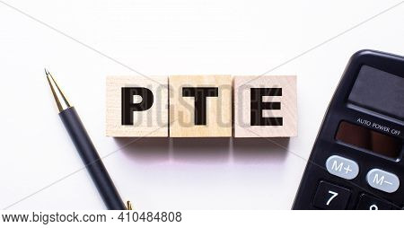 The Word Pte Is Written On Wooden Cubes Between A Pen And A Calculator On A Light Background.