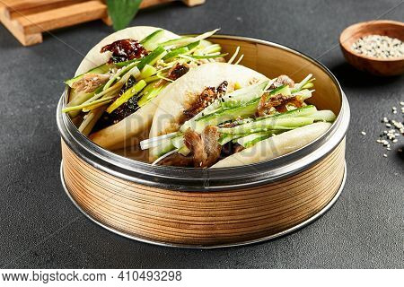 Bao bun with roast duck. Bamboo steamer on dark slate table. Chinese, asian, authentic food concept.