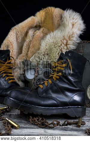 Leather Boots With Rusted Chains And Bullet Shells With Military Gas Mask And Fur Coat In Background