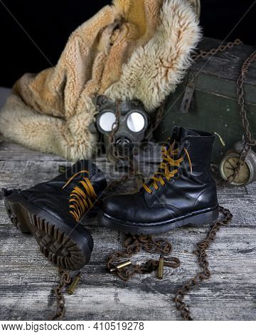 Leather Boots With Rusted Chains And Bullet Shells With Military Gas Mask And Fur Coat In Background