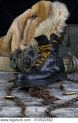 Leather Boot With Rusted Chains And Bullet Shells With Military Gas Mask And Fur Coat In Background
