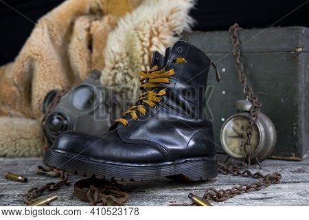 Leather Boot With Rusted Chains And Bullet Shells With Military Gas Mask And Fur Coat In Background