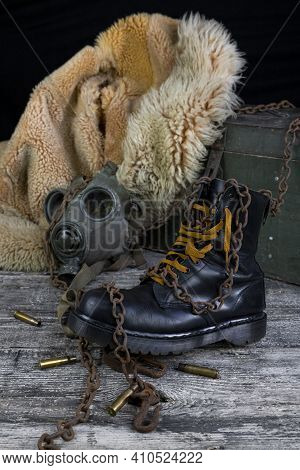 Leather Boot With Rusted Chains And Bullet Shells With Military Gas Mask And Fur Coat In Background
