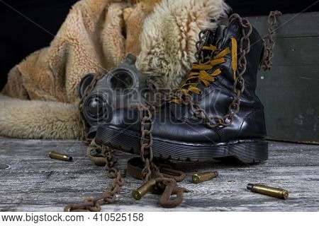 Leather Boot With Rusted Chains And Bullet Shells With Military Gas Mask And Fur Coat In Background