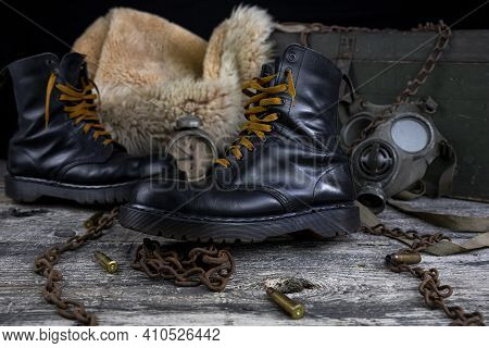 Leather Boots With Rusted Chains And Bullet Shells With Military Gas Mask And Fur Coat In Background