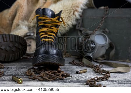 Leather Boots With Rusted Chains And Bullet Shells With Military Gas Mask And Fur Coat In Background