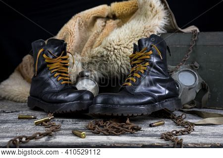 Leather Boots With Rusted Chains And Bullet Shells With Military Gas Mask And Fur Coat In Background