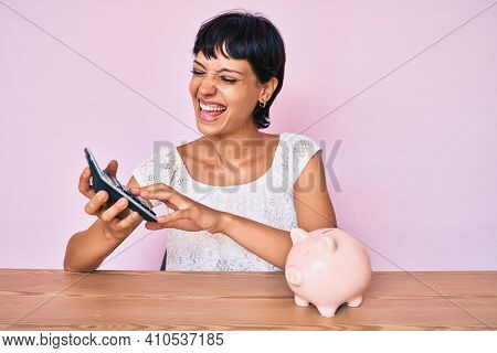 Beautiful brunettte woman caculating money savings smiling and laughing hard out loud because funny crazy joke. 