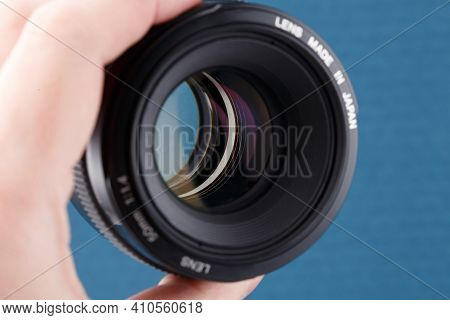 Hand Holding Modern Digital 50 Mm F 1.4 Dslr Lens On Blue Background - Close-up With Selective Focus