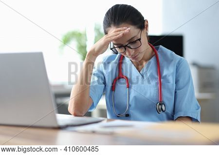 Tired Doctor Sitting At Table And Holding His Head. Medical Error Concept