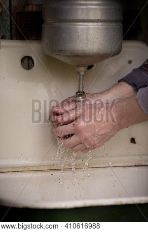 Wet Hands Of A Man Under The Washstand. An Old Rustic Washstand Hangs On The Wall. Metal Washbasin W