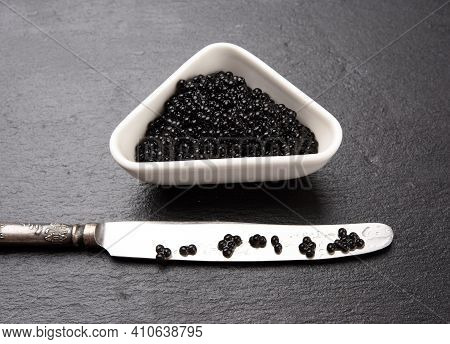 Black Grainy Caviar Of Paddlefish Fish In A White Ceramic Bowl, Black Background, Top View