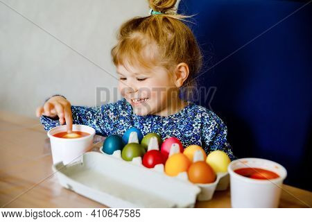 Excited Little Toddler Girl Coloring Eggs For Easter. Child Looking Surprised At Colored Egg Hoardin