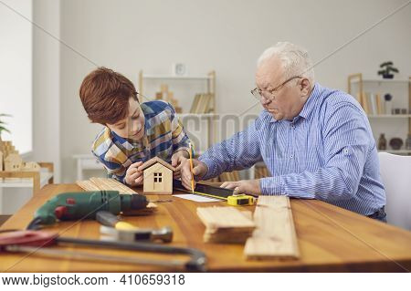Grandfather And Grandson Boy Making Wooden Birdhouse Together At Home
