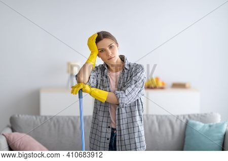 Cleaning Is So Dull. Bored Millennial Woman In Rubber Gloves Leaning On Mop, Tired Of Household Chor