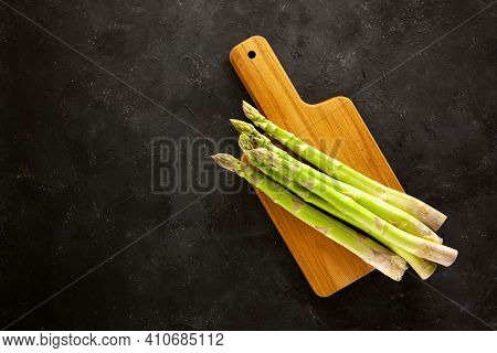 Bunch Of Asparagus On Wooden Cutting Board On Dark Gray And White Background.