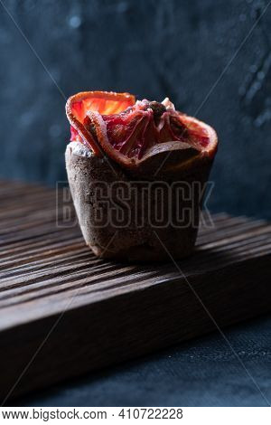 One Brownie Muffin With Blood Orange Slices On Ribbed Oak Cutboard On Dark Plaster Background Front 
