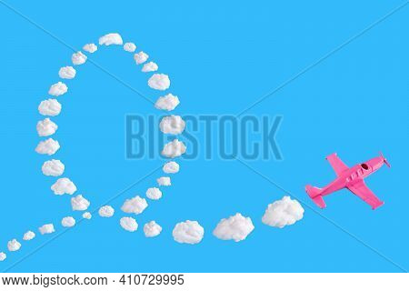 Pink Airplane Goes Into A Sharp Turn On Blue Background And Easter Egg Of Abstract Shapes Of Cloud. 