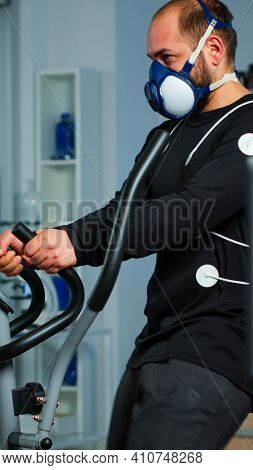 Monitor Showing Ekg Reading Of Athlete Running On Cross Trainer, While Medical Specialists Supervise