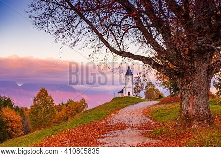 Beautiful Sunset Landscape Of Church Jamnik In Slovenia On Green Hill With The Trees And Pink Sky
