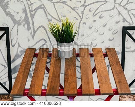 Indoor Artificial Flower In White Grey Pot On Wooden Blank Empty Table In Cafe By The Wall