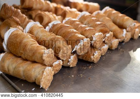 On A Metal Board Lie Puff Pastry Rolls With Protein And Custard, Sprinkled With Powdered Sugar. Puff